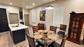 A modern kitchen with a central island, a dining area with a glass table and woven placemats, and a decorative door with intricate metalwork.
