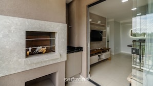 A modern kitchen with a built-in oven, a glass door leading to a balcony, and a flat-screen TV mounted on the wall. - 2BR apt w/ BBQ 750m From Beach Rvn2003 (Itapema)