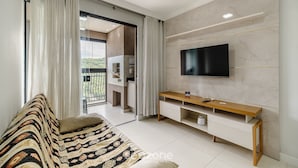 A modern living room with a sofa, TV, and a sliding glass door leading to a balcony. - 2BR apt w/ BBQ 750m From Beach Rvn2003 (Itapema)