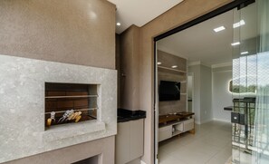 A modern kitchen with a built-in oven, a glass door leading to a balcony, and a flat-screen TV mounted on the wall.