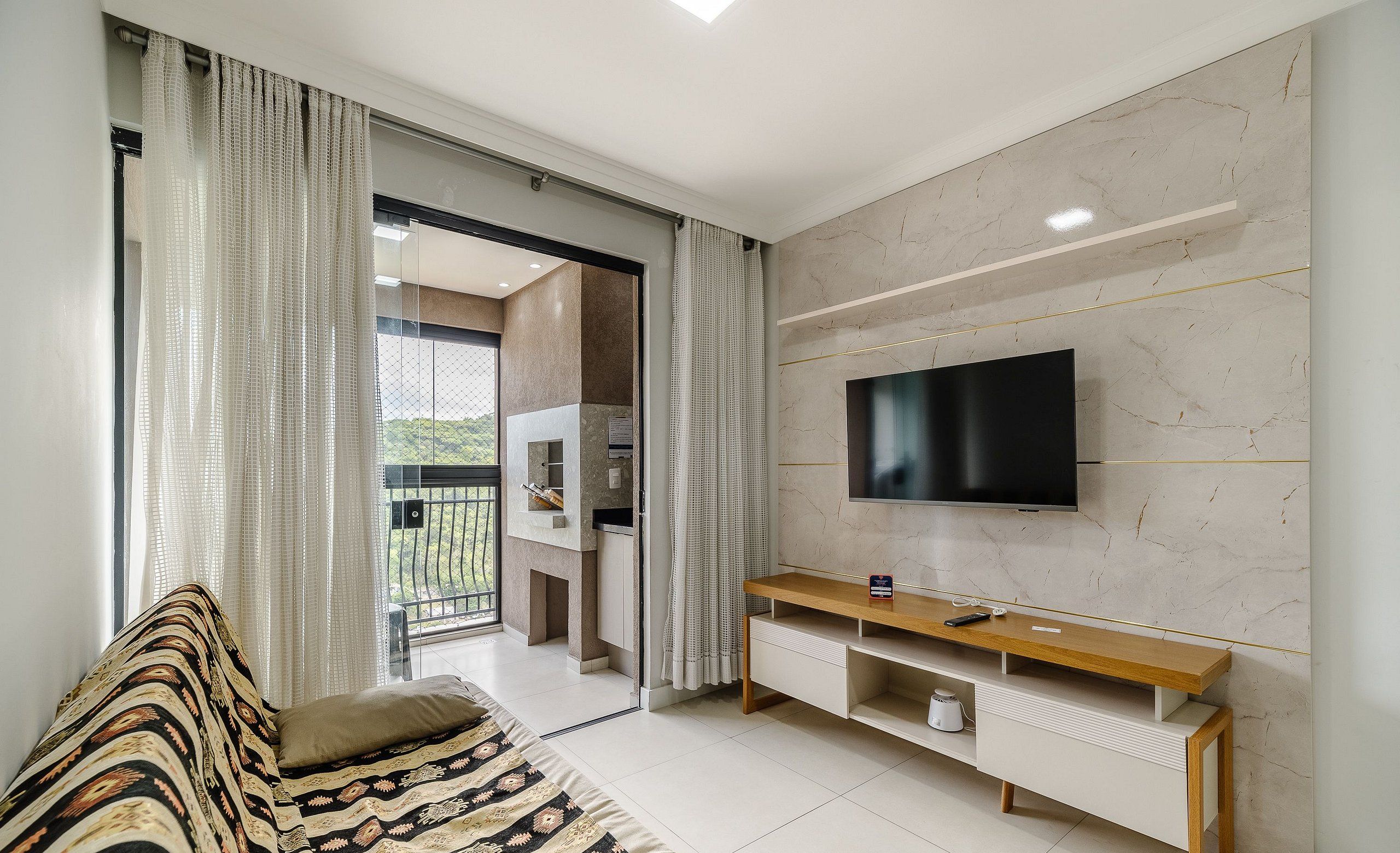 A modern living room with a sofa, TV, and a sliding glass door leading to a balcony.