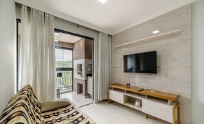 A modern living room with a sofa, TV, and a sliding glass door leading to a balcony.