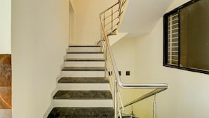 A staircase with a metal railing, white walls, and a window with blinds. - Collection O Hotel Sp14 (Indore)