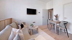A modern living room with a sofa, a coffee table, a TV, and a dining area with chairs and a table. - The Gallery Studio at Bramham Gardens (London)