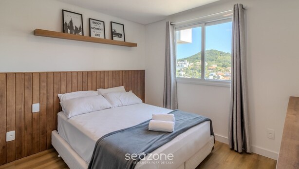 Une chambre à coucher avec une tête de lit en bois, un lit recouvert de draps blancs, une couverture grise et une fenêtre avec des rideaux.