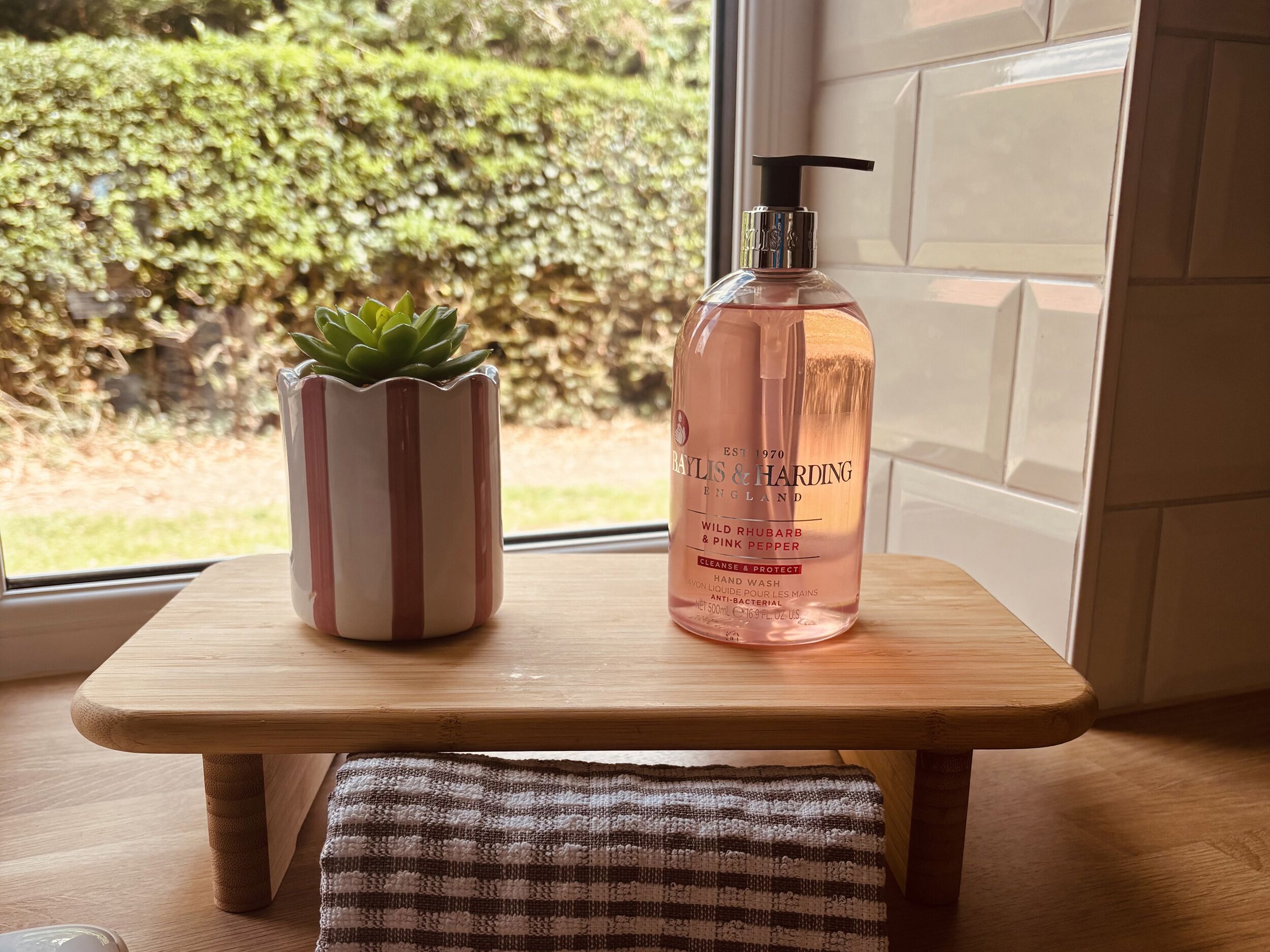 Une petite table en bois, sur laquelle se trouvent un flacon de savon pour les mains de la marque Baylis & Harding et une petite plante succulente en pot.