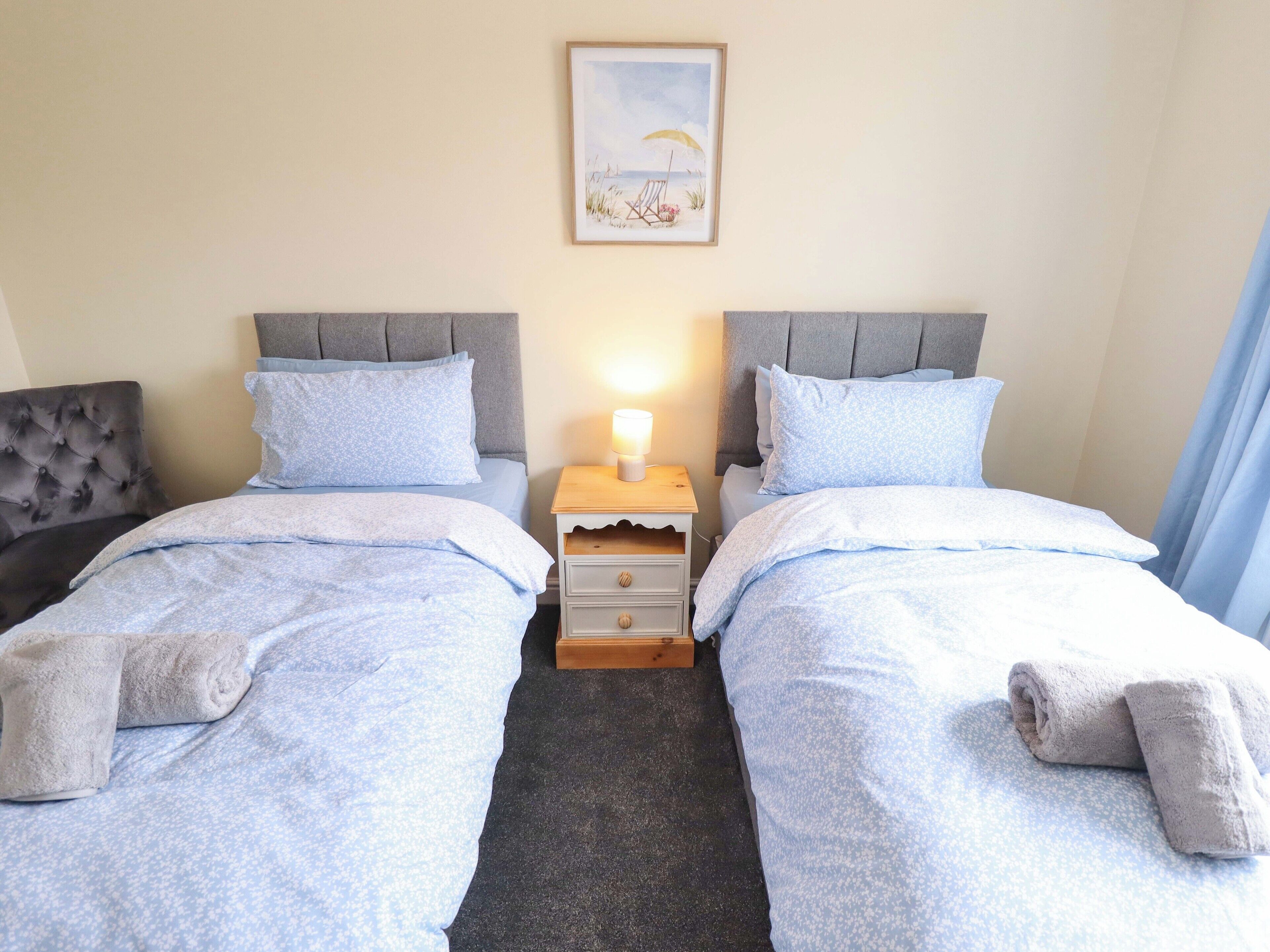 Habitación doble con dos camas, una mesita de noche con lámpara, un cuadro en la pared y una silla.
