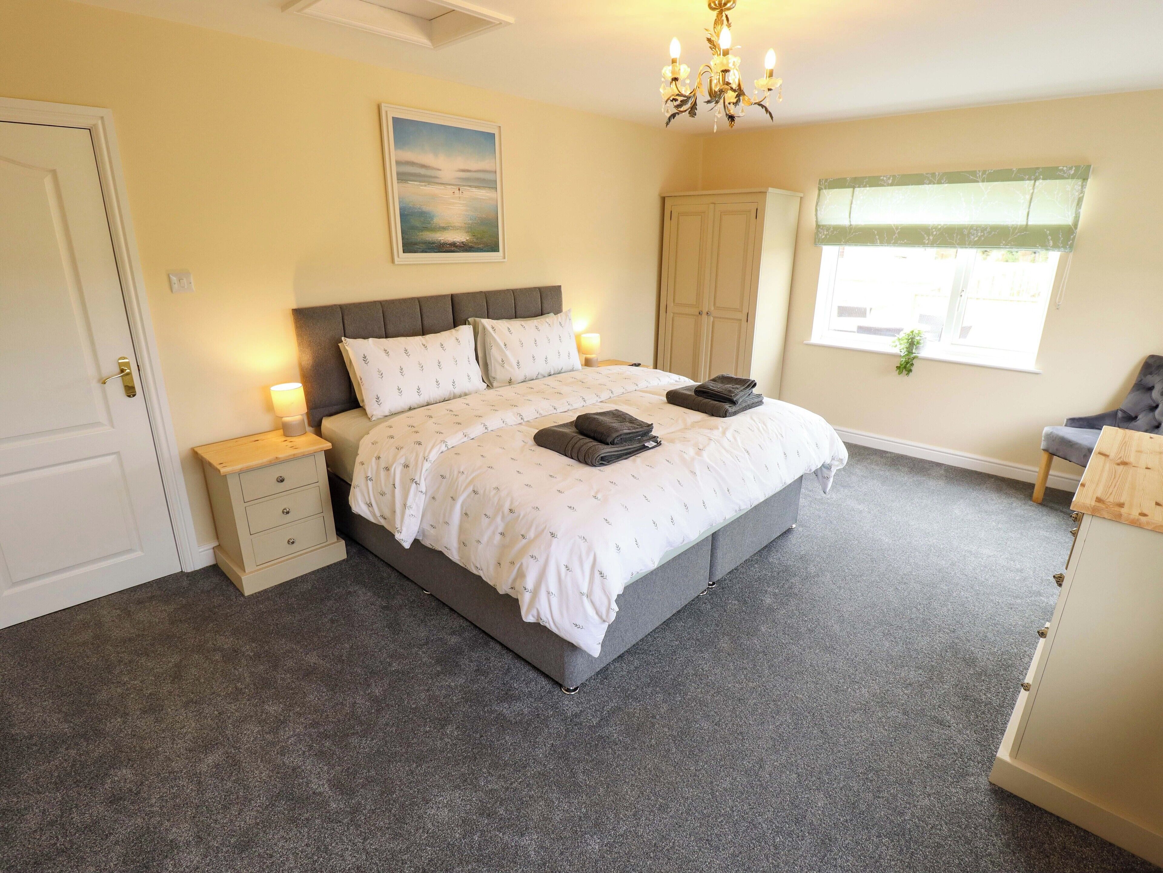 A bedroom with a bed, bedside tables, a wardrobe, a window, and a chandelier.