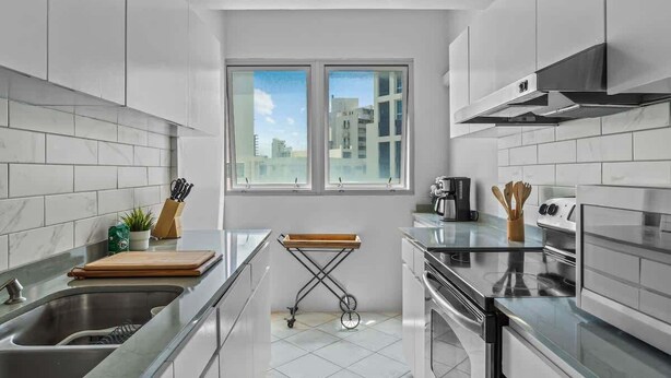 Una cocina moderna con armarios blancos, un lavamanos de acero inoxidable y una ventana que ofrece luz natural.