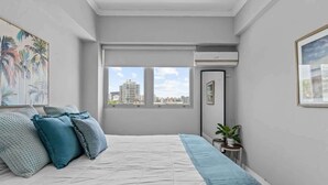 Un dormitorio con una cama, un ventanal con vistas a la ciudad y una mesita con una planta.
