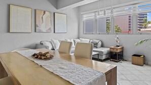 Una sala moderna con un sofá, una mesa de comedor con un mantel individual y una ventana con persianas.