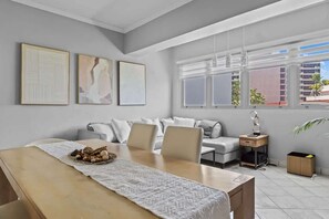 Una sala moderna con un sofá, una mesa de comedor con un mantel individual y una ventana con persianas.