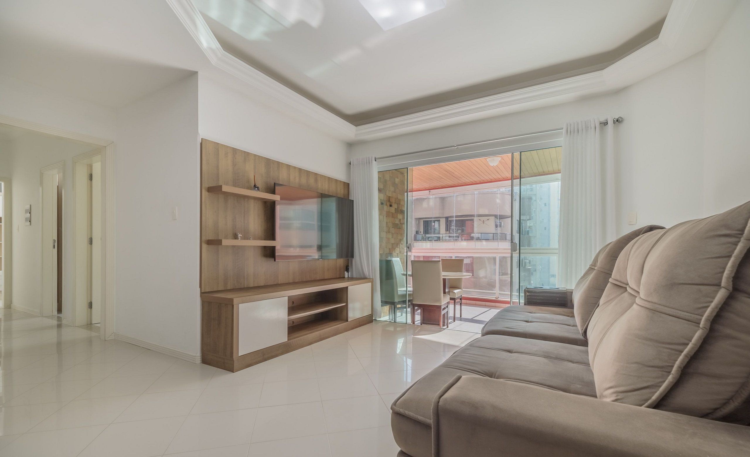 A modern living room with a large sofa, built-in entertainment unit, and a balcony with a view.