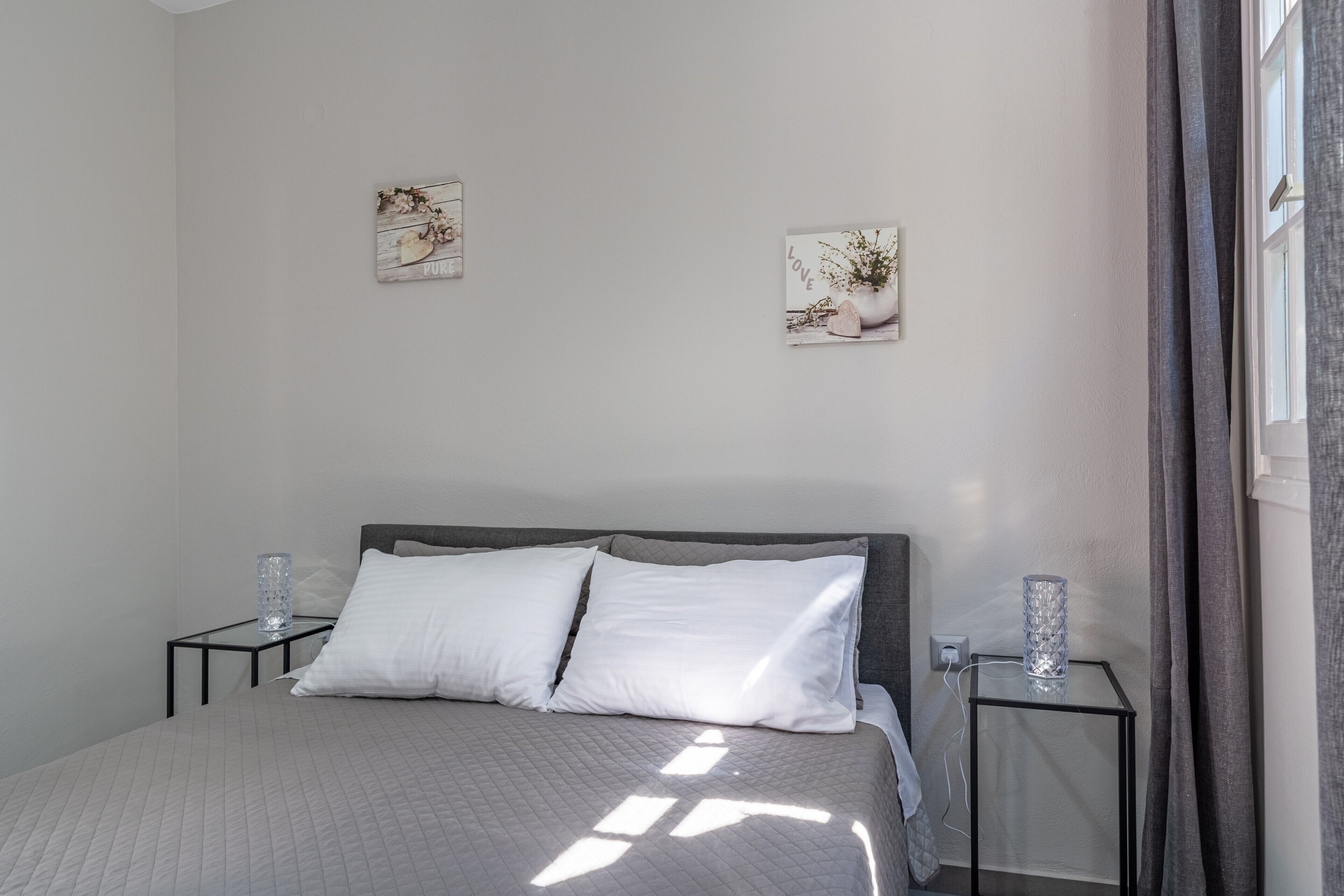 Une chambre à coucher bien rangée, avec un lit, deux tables de chevet et deux œuvres d’art accrochées au mur.