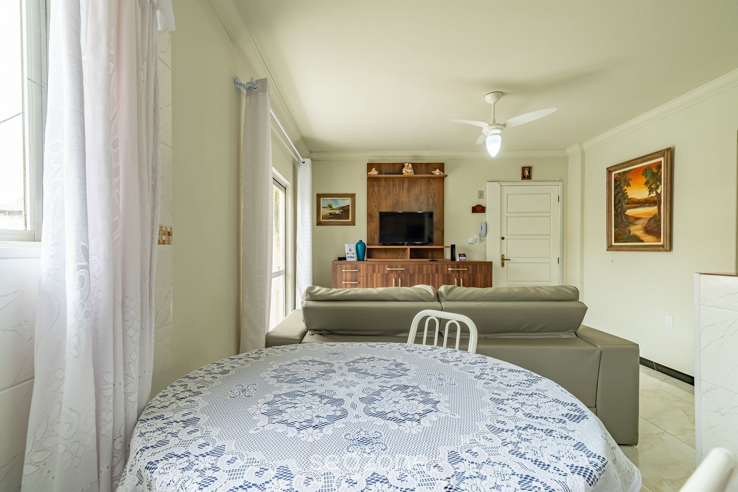 A living room with a sofa, a television, and a dining table with a patterned tablecloth.