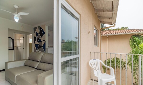 A modern living room with a sofa, a ceiling fan, and a sliding glass door leading to a balcony with a white chair. - 2BR Apt 260m From Canto Beach Itapema Rtl0302 (Itapema)