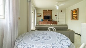 Uma sala de estar com sofá, televisão e mesa de jantar com toalha de mesa estampada.