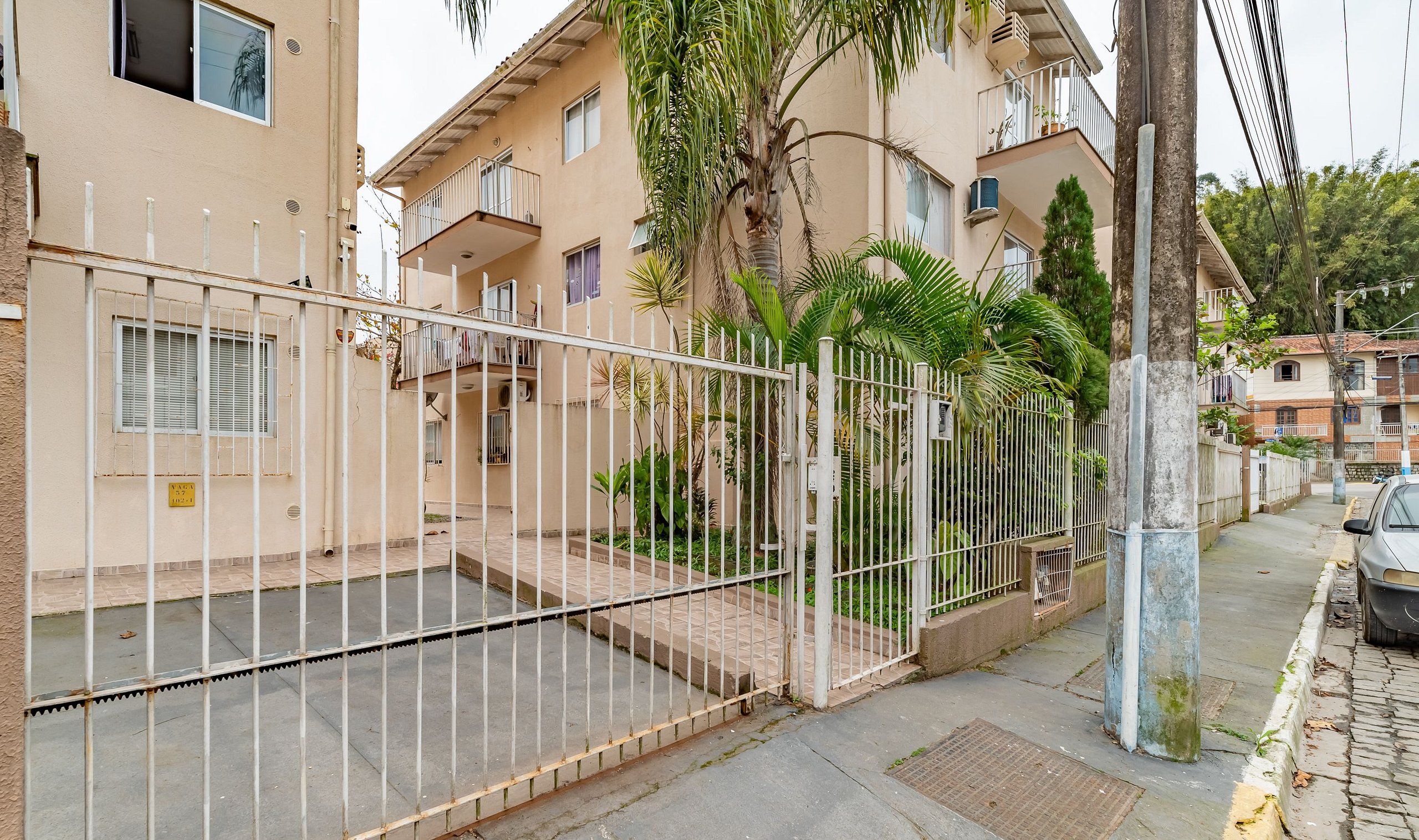 A residential building with a gated entrance, a balcony, and a palm tree.