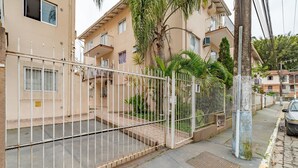 Um edifício residencial com portão fechado, varanda e uma palmeira.