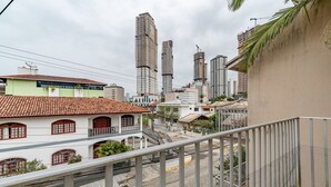 Paisagem urbana com edifícios altos, uma combinação de estruturas residenciais e comerciais, e uma varanda com guarda-corpo de metal.