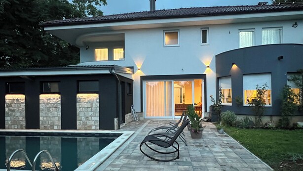 Een modern huis met een zwembad, een terras en een verzorgde tuin.