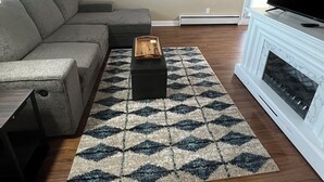 Un salón con un sofá modular, un televisor de pantalla plana, una chimenea y una alfombra estampada.