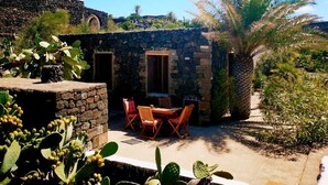 Un edificio de piedra con un patio, asientos exteriores y una palmera.