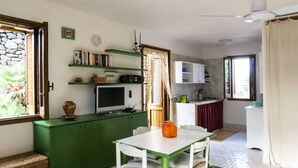 Cocina compacta con comedor, muebles verdes, una mesa blanca y un televisor sobre un mueble verde.