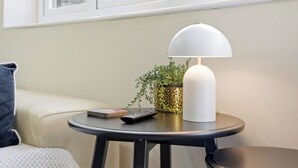 Una mesa redonda con una lámpara blanca, un control remoto y una planta en maceta.