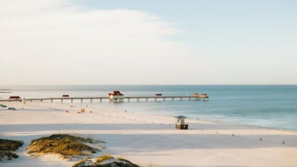 A beach with a pier extending into the water, featuring several structures along its length.
