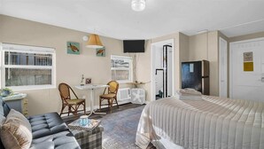 A compact bedroom with a bed, a sofa, two chairs, a small table, and a TV.
