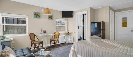 Un dormitorio compacto con cama, sofá, dos sillas, una mesita y televisor.