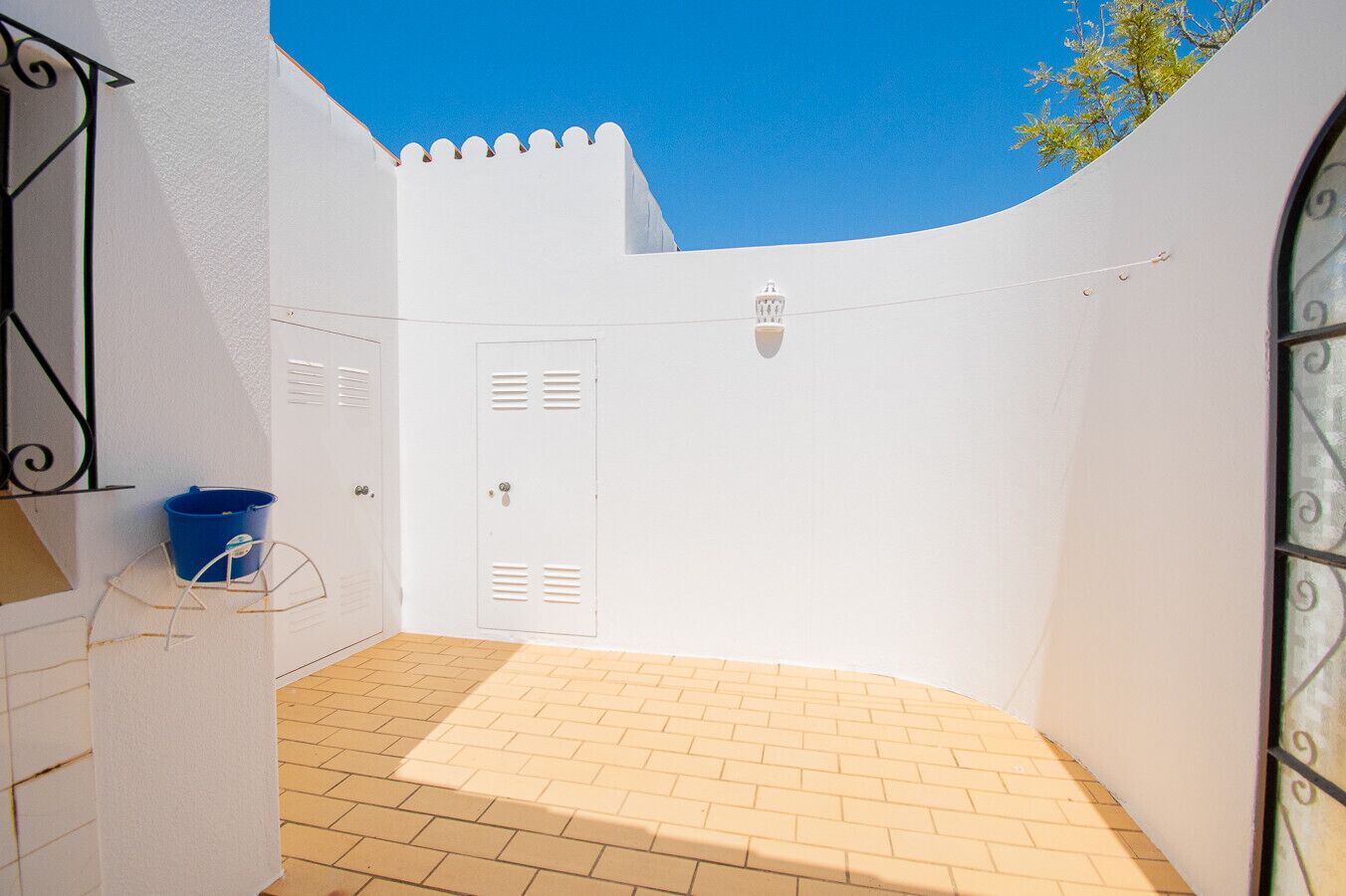 A small enclosed patio with a tiled floor, white walls, and a blue bucket.
