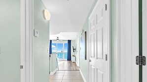 Een gang met lichtgroene muren, witte deuren en een betegelde vloer, leidend naar een balkon met uitzicht op zee.