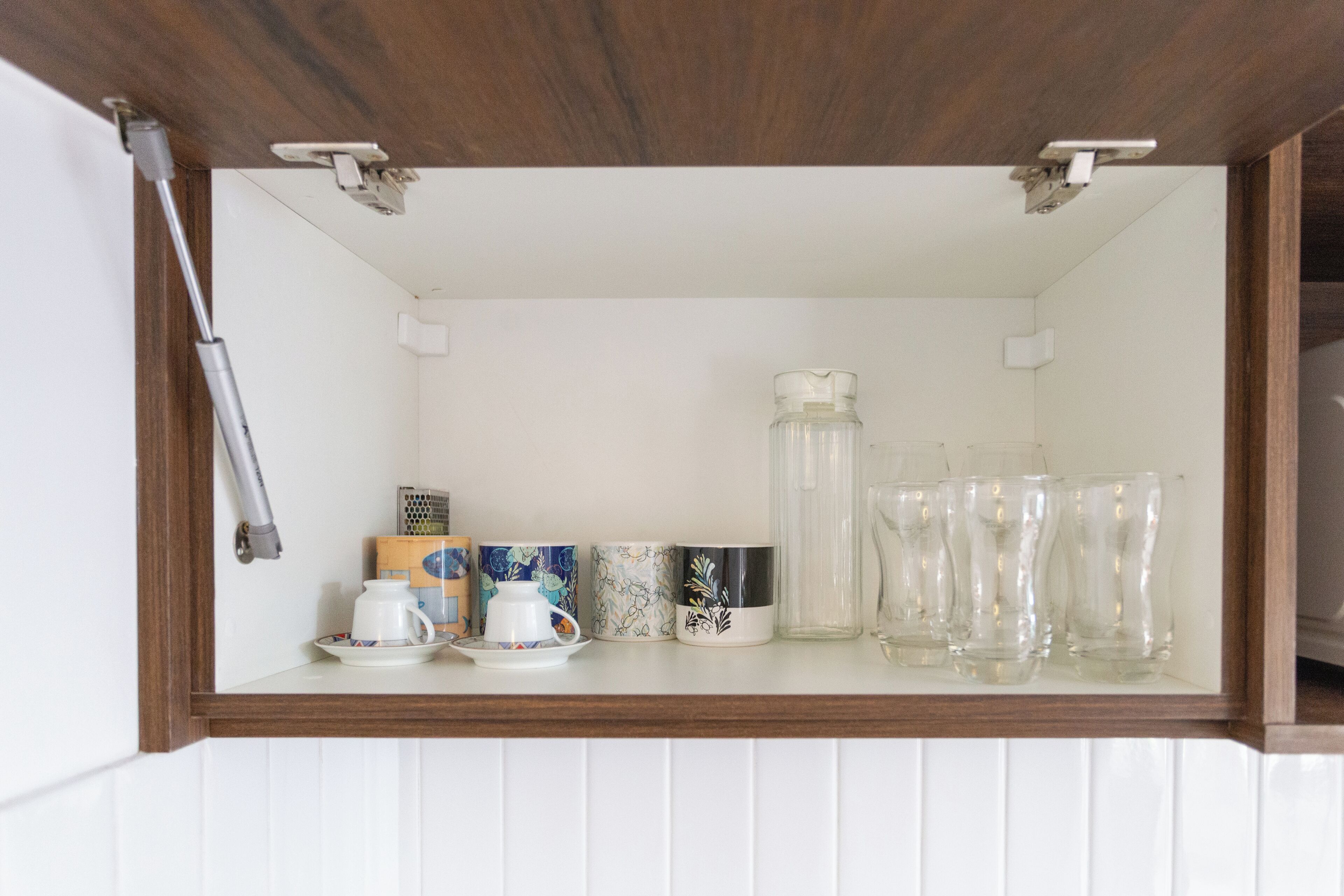 Un armario de cocina con interior blanco, encimera de madera y varios utensilios de cocina, incluyendo una cafetera, tazas y un tarro de vidrio.
