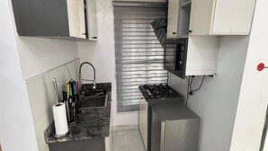 A compact kitchen with a gas stove, a microwave, and a stainless steel sink. There is a fire extinguisher on the floor.