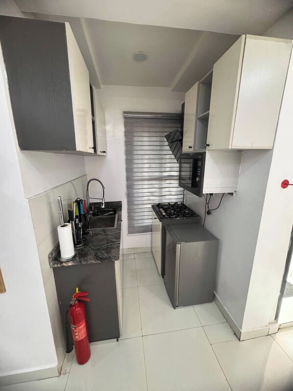 A compact kitchen with a gas stove, a microwave, and a stainless steel sink. There is a fire extinguisher on the floor. - Topaz Chic 1-bedroom apartment in vibrant Ikeja with AC (Ikeja)