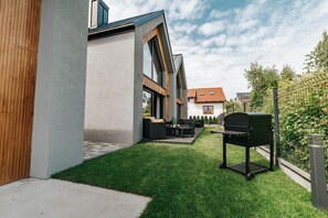 A modern outdoor patio with a barbecue grill, seating area, and a well-maintained lawn.