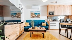A modern living room with a blue sofa, wooden cabinets, a kitchen area, and a dining table.