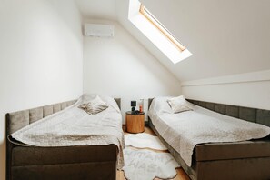 Alojamiento pequeño y de una sola habitación con dos camas, un tragaluz, un radiador y una mesita auxiliar.