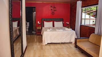 Quarto de hotel com uma cama grande, um sofá, um espelho e vista para o exterior.