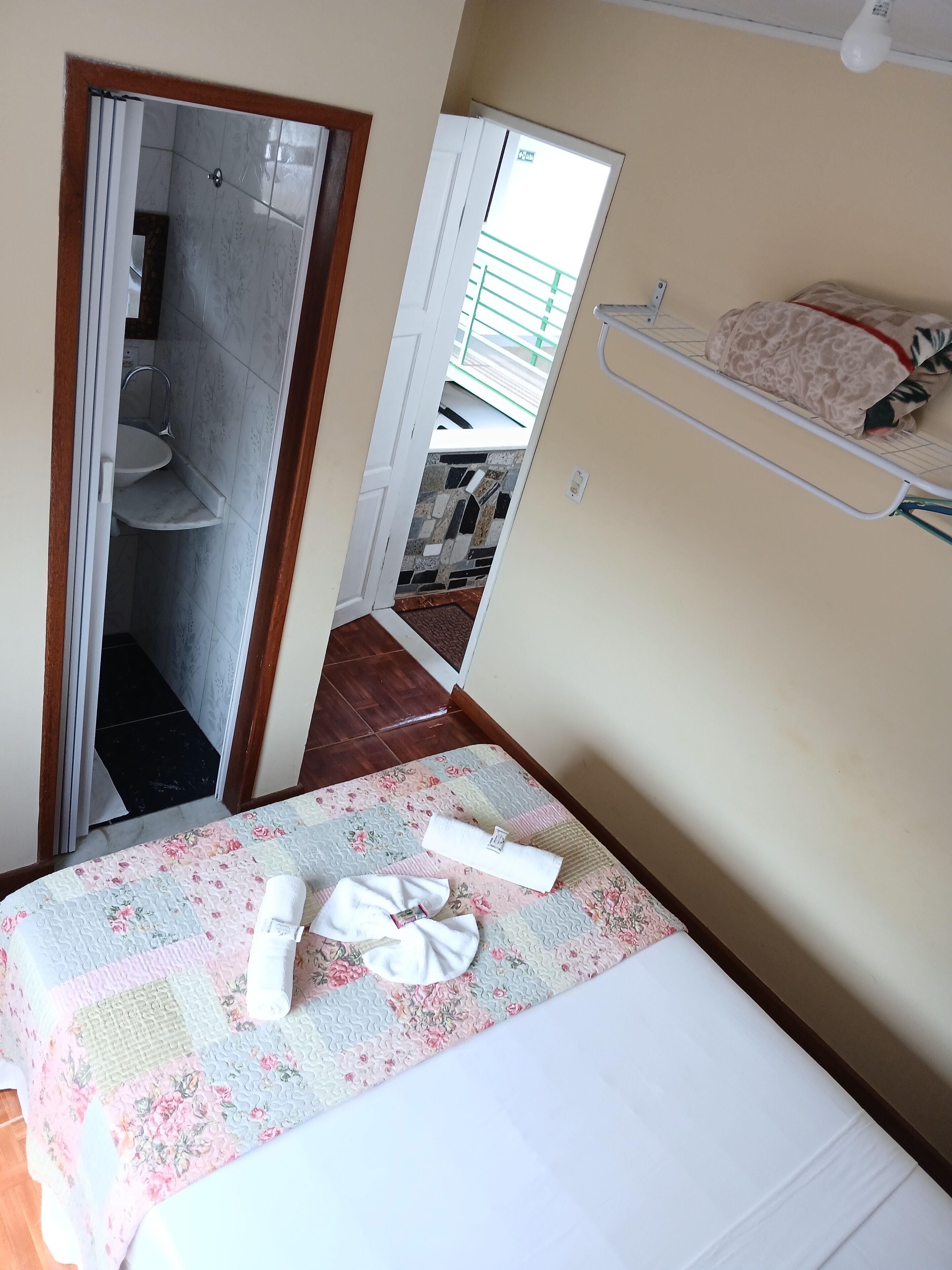 Ett hotellrum med en säng, ett badrum som syns genom en öppen dörr, en liten hylla med handdukar och ett fönster med utsikt över en balkong.