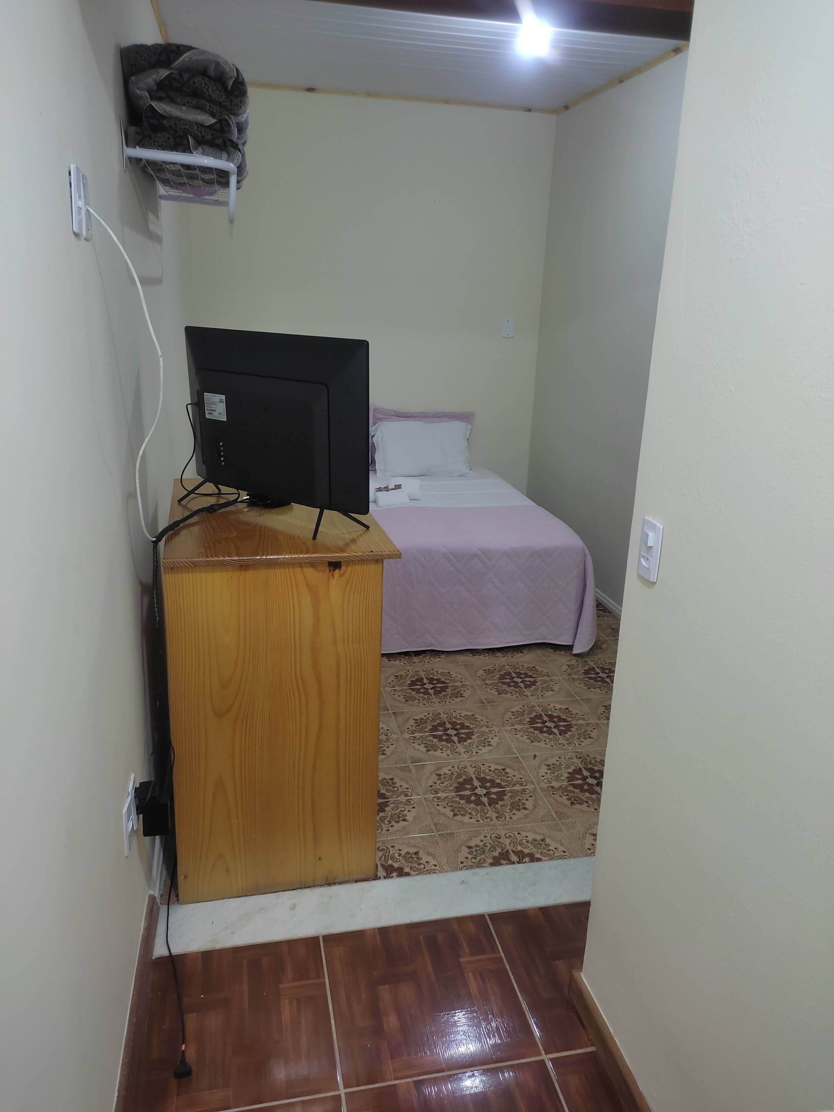 A small room with a bed, a desk with a computer, and a wall-mounted shelf.