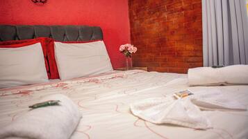 A neatly made bed with white and red bedding, a vase with pink flowers, and a brick wall in the background.