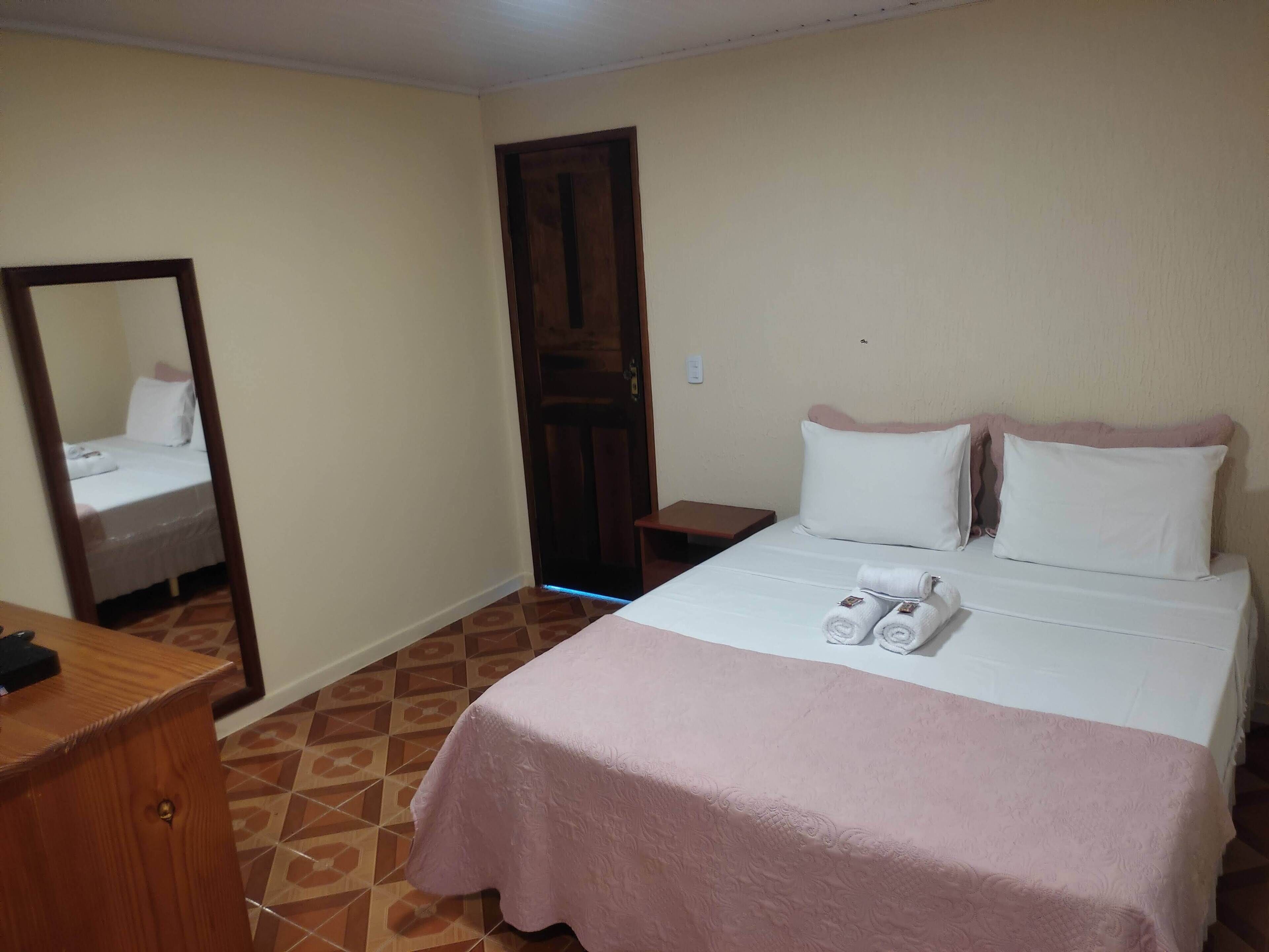 Una habitación de hotel con una cama, una mesita de noche de madera, un espejo y una puerta.