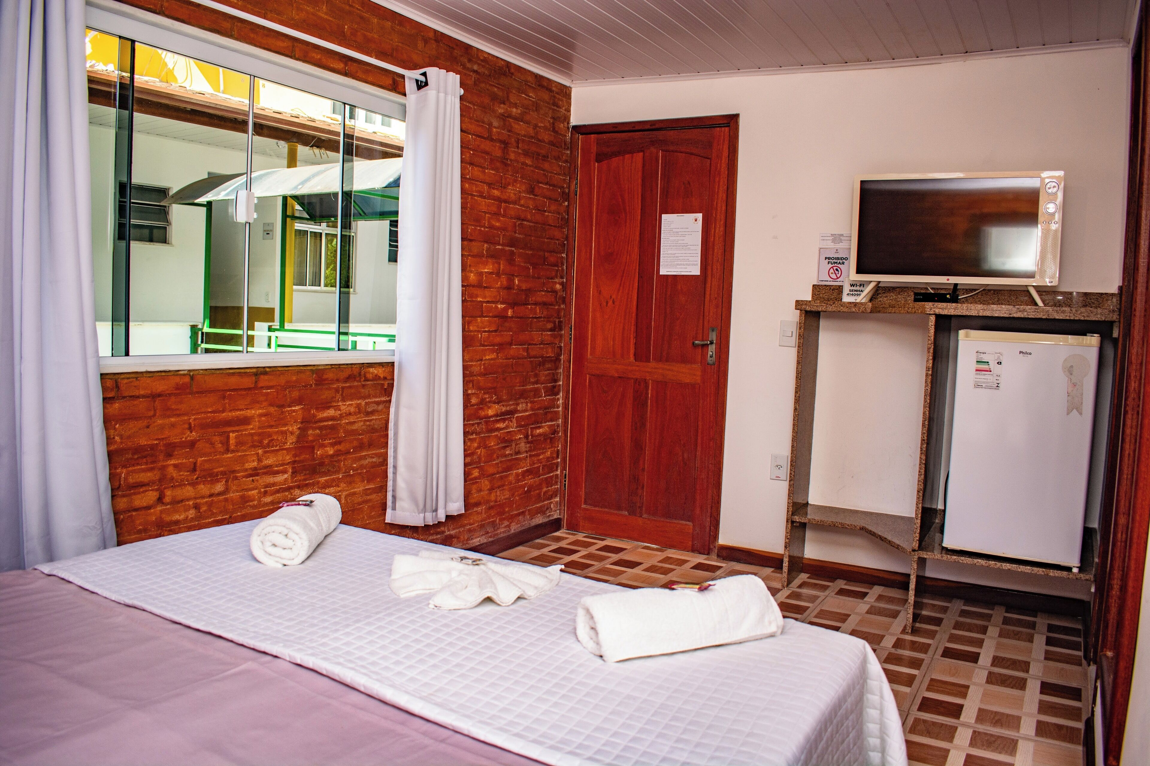 Una habitación de hotel con cama, televisor, refrigerador y puerta de madera.