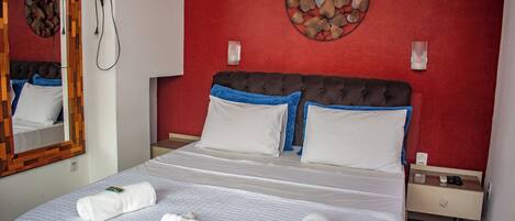 A hotel room with a bed, a nightstand, a mirror, a wall decoration, and a hairdryer on the wall.