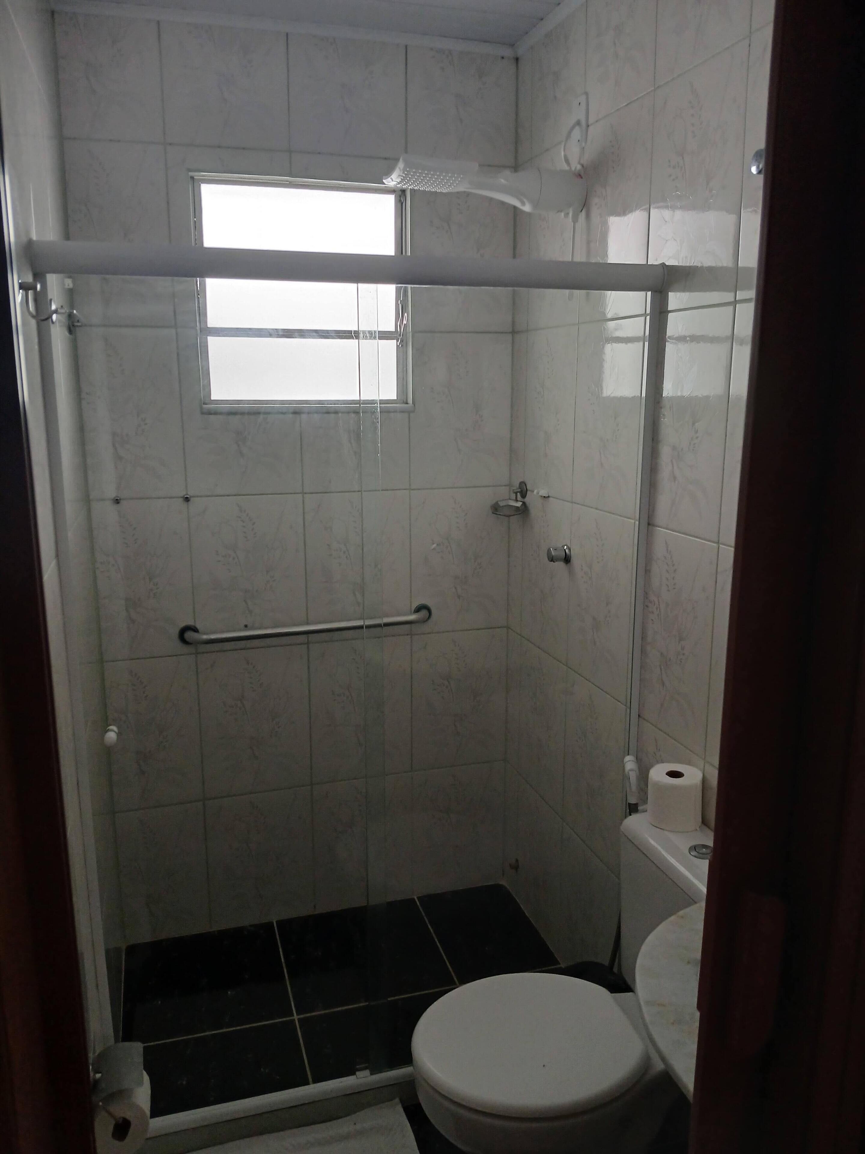 A bathroom with a shower, toilet, and a window.