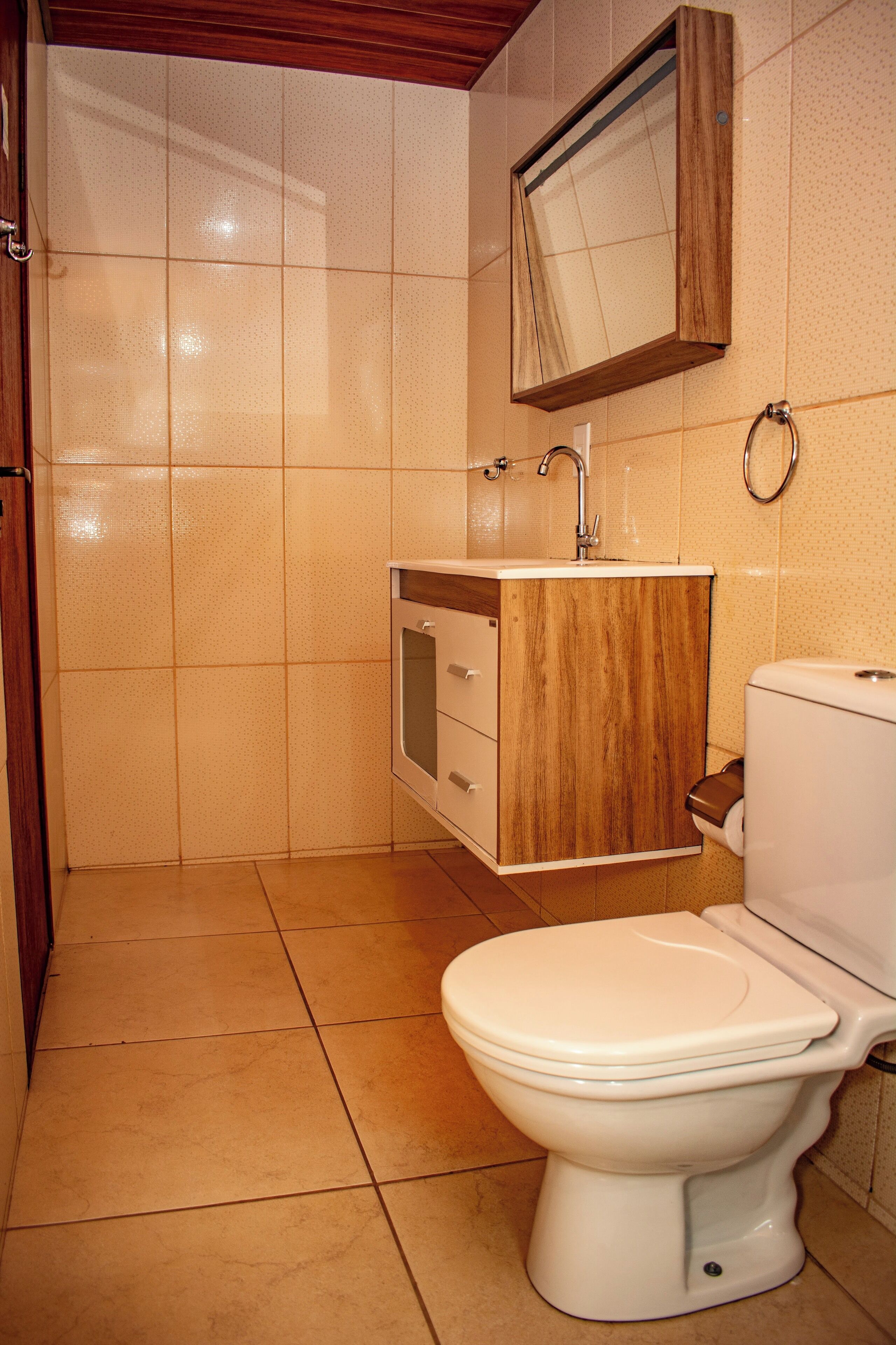 Een badkamer met toilet, een houten wastafelmeubel, een spiegel en betegelde wanden.