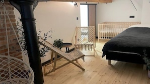 Ein Zimmer mit einem Bett, Holzboden, einem Korbstuhl, einem kleinen Tisch und einem Babybett.